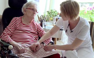 Kvindelig social- og sundhedsassistent taler med ældre kvinde i kørestol